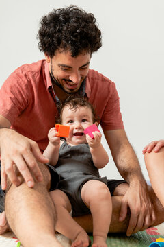 Joyful young father with baby playing together with toys sitting on mat