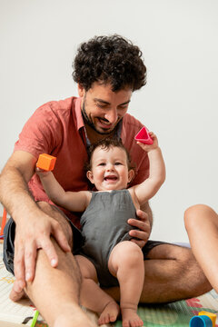 Joyful young father with baby playing together with toys sitting on mat