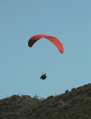 Paraglider with a red parachute flying above hills