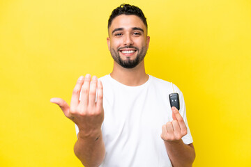 Young Arab man holding car keys isolated on yellow background inviting to come with hand. Happy...