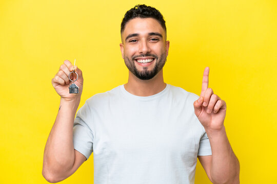 Young Arab Man Holding Home Keys Isolated On Yellow Background Pointing Up A Great Idea