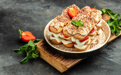 Tiramisu. Homemade tiramisu cake with fresh strawberry, mascarpone and mint. Tiramisu portion on plate on dark background. Delicious no bake tiramisu