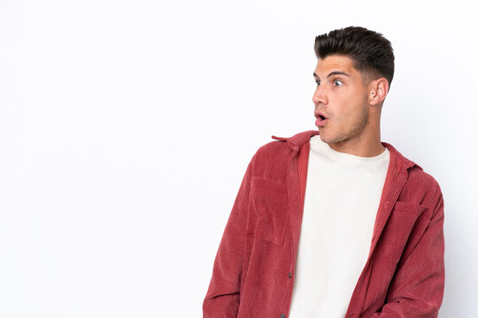 Young caucasian man isolated on white background doing surprise gesture while looking to the side