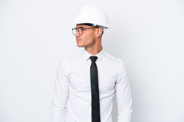 Young architect caucasian man with helmet and holding blueprints isolated on white background looking to the side