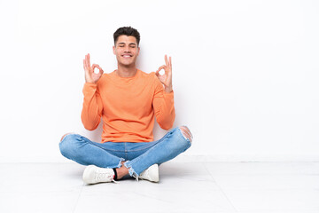 Young man sitting on the floor isolated on white background in zen pose