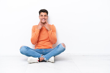 Fototapeta na wymiar Young man sitting on the floor isolated on white background smiling with a happy and pleasant expression