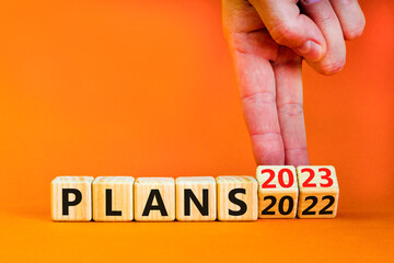 2023 plans new year symbol. Businessman turns a wooden cube and changes words Plans 2022 to Plans 2023. Beautiful orange table orange background, copy space. Business 2023 plans new year concept.