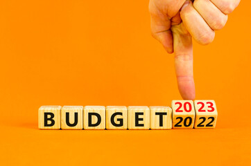 Planning 2023 budget new year symbol. Businessman turns a wooden cube and changes words Budget 2022 to Budget 2023. Beautiful orange background, copy space. Business 2023 budget new year concept.