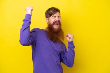 Redhead man with beard isolated on yellow background celebrating a victory
