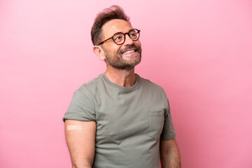 Middle age man wearing a band aids isolated on pink background looking up while smiling