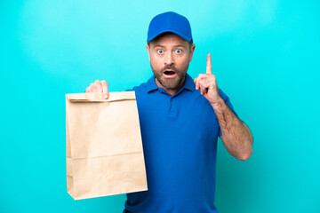 Middle age man taking a bag of takeaway food isolated on blue background thinking an idea pointing...