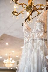 Blush lace bridal gown hanging from a glass chandelier in reception area with ceiling lights in background