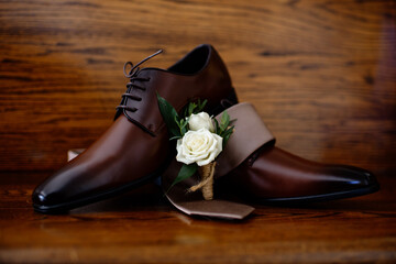 Simple white rose boutonnière upon men's dress shoe sitting on a church pew