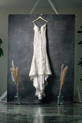 Wedding dress hanging in front of a grey Oliphant backdrop with sprays of pampas grass