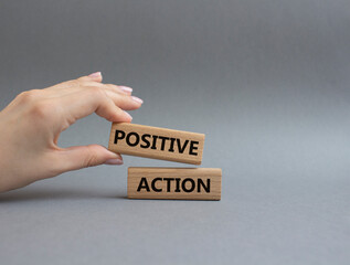 Positive action symbol. Concept words Positive action on wooden blocks. Beautiful grey background. Businessman hand. Business and Positive action concept. Copy space.