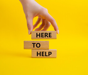 Here to help symbol. Wooden blocks with words Here to help. Beautiful yellow background. Businessman hand. Business and Here to help concept. Copy space.