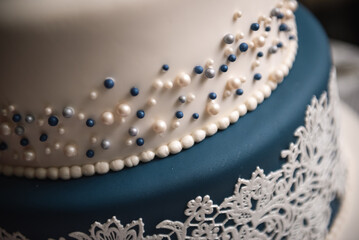 Blue and white iced wedding cake with blue and white pearl beads and ruffled icing topped with a bride and groom figurine and lace edging