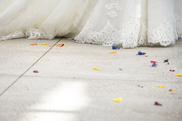 Bottom of a wedding dress trailed with colorful rose petals on the floor