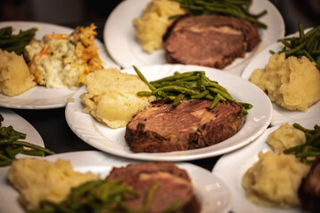 Plates stacked up on another with slices of prime rib, sautéed green beans and mashed potatoes at a wedding reception
