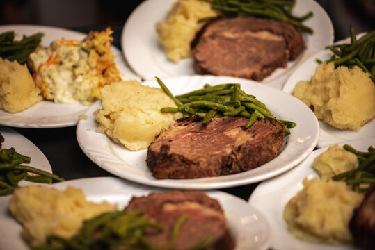 Plates Stacked Up On Another With Slices Of Prime Rib, Sautéed Green Beans And Mashed Potatoes At A Wedding Reception