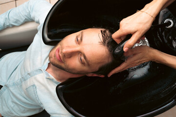 Hair salon master washing client hair at barber shop. Male client getting haircut by hairdresser. Hair care, beauty industry, barber concept