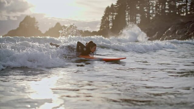 Surf girl catches wave at picturesque tofino beach during sunset