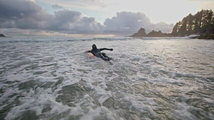 Surf girl jumps on board and paddles through water at picturesque Vancouver Island beach at sunset