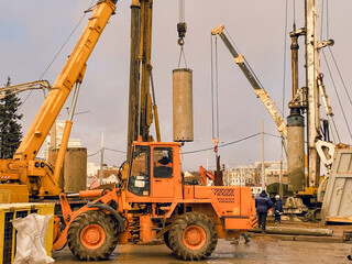 construction equipment at the overpass repair site. large concrete blocks are erected by cranes. an orange tractor for asphalt paving drives nearby on large wheels