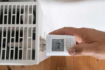 Hand turns the radiator thermostat to the minimum due to rising gas prices. Concept of energy...