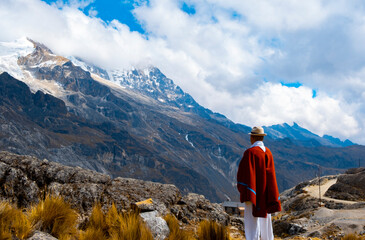 indigenous man in red poncho looking at the mountains in the andes