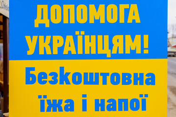 The inscription in Ukrainian Help Ukrainians free food and drinks. Ukrainian flag background with selective focus