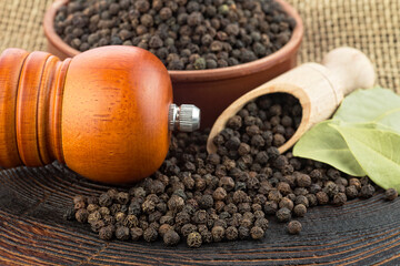 Wooden pepper mill, laurel leaves and black peppercorns on a wooden table.