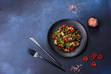 A salad of baked aubergine, sweet pepper, garlic, zucchini and parsley in a black plate