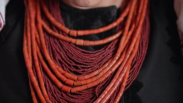 Ukrainian woman puts on authentic jewelry - coral beads. She is in national costume of Ukraine - vyshyvanka. Folk handmade necklace in traditional style.