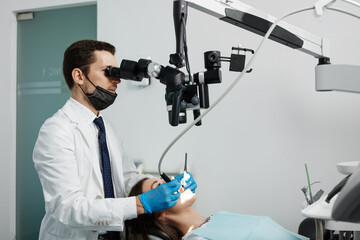 Male dentist using dental microscope in dental office with female patient