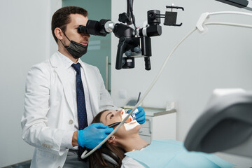 Male dentist using dental microscope in dental office with female patient