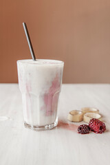 Blackberry and banana smoothie served in a glass cup on a white wooden table. Blackberries and banana on the sides of the glass