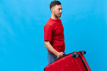 Cheerful confident tanned handsome man in red t-shirt going with suitcase ready for vacation trip...