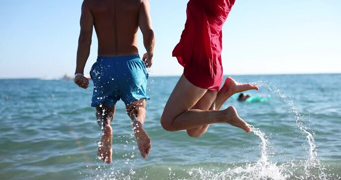 Happy married couple are jumping in water at sea