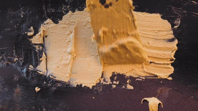 A man's hand with a spatula applies putty to the worn paint of a car. Medium plan