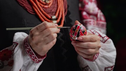Ukrainian woman painting traditional ornamets on Easter egg - pysanka. Artist working in national costume. Preparation for Christian holiday
