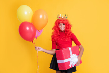 smiling girl in crown with present box and party balloon on yellow background