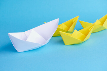 A big white paper boat leads small yellow paper boats as a team. Concept for teamwork, cooperation,...
