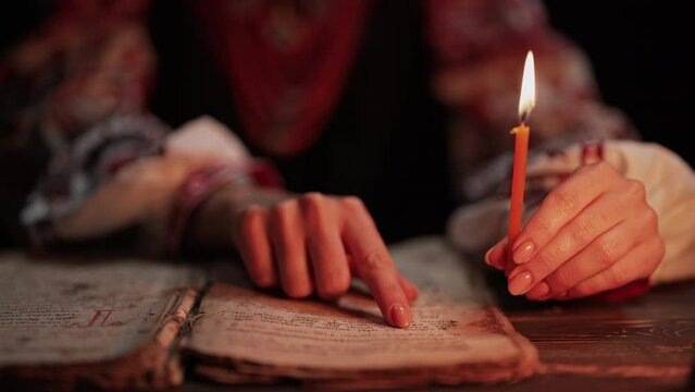 Ukrainian woman reading ancient book - Bible. Concentrated attentively follows finger on paper page under candle light. History of Kyiv Rus. Psalter, 19th century, prayers and psalms