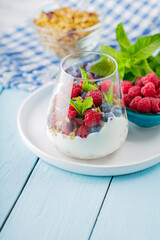 Healthy meal made of granola, yogurt and fruits on painted boards. Diet dessert with yogurt, granola and pomegranate fruit in a glass. Healthy breakfast on a blue surface