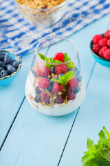 Healthy meal made of granola, yogurt and fruits on painted boards. Diet dessert with yogurt, granola and pomegranate fruit in a glass. Healthy breakfast on a blue surface