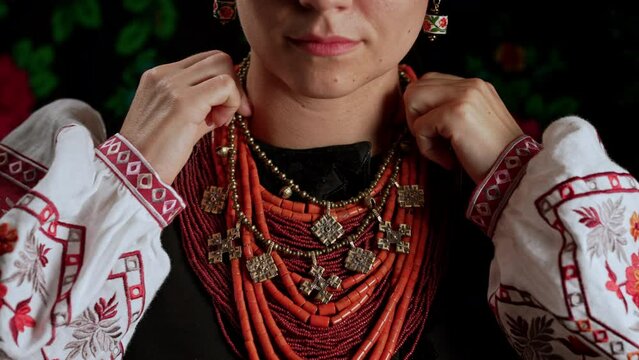 Woman corrects traditional antique jewelry necklace. Ukrainian model in national costume - vyshyvanka and ancient coral beads, Zgarda - archaic hutsul neck ornament of status religious purpose