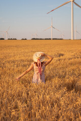 Beautiful girl at sunset in a wheat field with windmills to generate electricity. The concept of renewable energy, love for nature, electricity. Renewable energy.