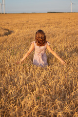 Fototapeta na wymiar Beautiful girl at sunset in a wheat field with windmills to generate electricity. The concept of renewable energy, love for nature, electricity. Renewable energy.