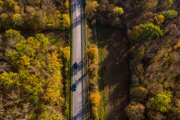 A road with several cars through a German mixed forest seen from the air in autumn